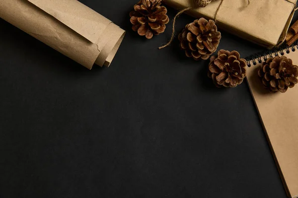 Black background with pine cones , cropped Christmas Gift in craft wrapping paper in the corner of the image. Flat lay, copy space