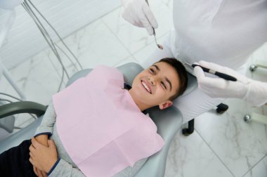 Pediatrik diş hekimliği kliniğinde diş muayenesi sırasında dişçi koltuğunda gülümseyen bir çocuğun genel görünüşü. Erken teşhis konması ve diş hastalıklarının zamanında tedavi edilmesi