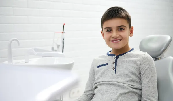 可爱的青春期前男孩坐在牙医的椅子上接受定期的医疗预防检查 微笑着看着相机 健康生活方式概念 — 图库照片