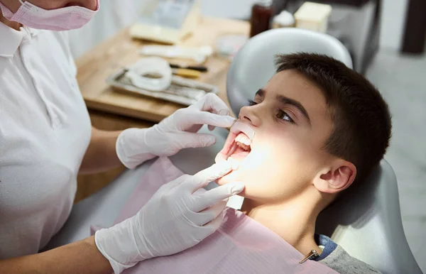 歯科口腔治療中に歯科医を見て 歯科医の椅子に座って彼の口の中に頬のリトラクターと自信のある子供の少年のクローズアップ 口腔衛生 医療の概念 — ストック写真