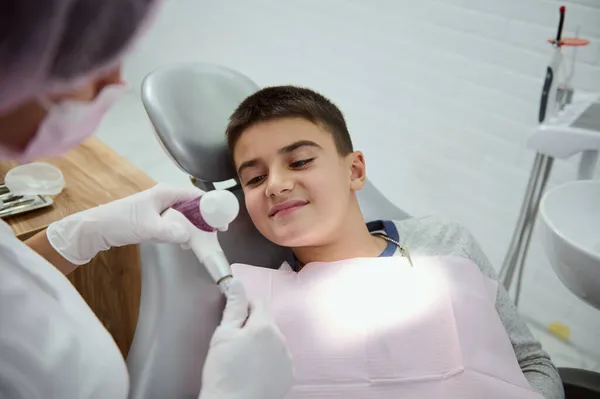 愛らしいハンサムな子供 小児歯科医の訪問中に歯科医の椅子に座っている学校の少年は 近代的な白い歯科医院で 医療口腔治療を受けています 歯科口腔衛生の概念 — ストック写真