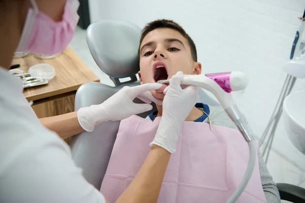小児科の歯科医は 白い現代的な歯科事務所で定期的な医療検査で医師の訪問中に歯医者の椅子に座っているハンサムな男の子の子供の歯のケアと口腔を扱います — ストック写真