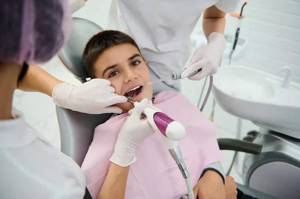 歯医者の診察中に歯医者の椅子で勇敢な学校の少年 小児歯科クリニックで歯の治療を受けます ケアの早期診断と歯科疾患のタイムリーな治療の概念 — ストック写真