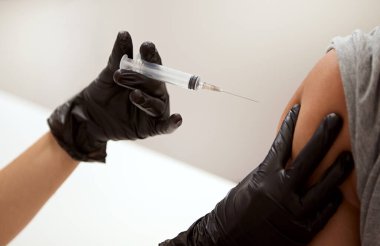 Korunaklı steril eldivenli sağlık çalışanlarının elinde antiviral aşı şırıngası var ve Corona virüsü enfeksiyonu ve bulaşıcı hastalıkların yayılması için enjeksiyon yapıyorlar.