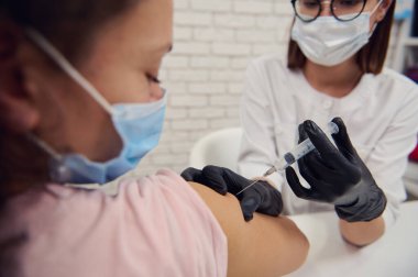 Siyah saçlı, koruyucu maskeli bir kadın Corona virüsü aşısıyla aşılanıyor. Bulaşıcı viral hastalıkların yayılması için gönüllü aşı kavramı. Nüfusun dokunulmazlığı