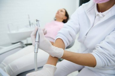 Diş hekimlerinin dişçi koltuğunda yatan kadın bir hastanın arka planındaki diş matkabının yakın çekimi. Dişçi konsepti. Diş muayenehanesinde diş matkabını kullanan dişçi görüntüsü