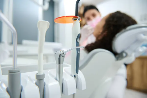 Focus on modern dental equipment used in dentistry on the background of blurred dentist using modern special ultraviolet light lamp for teeth whitening procedure.