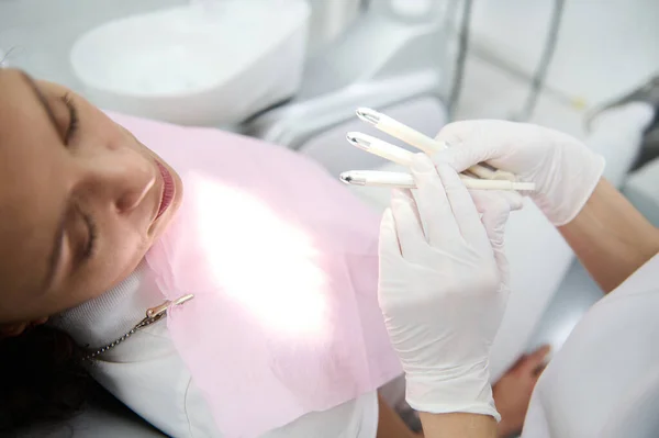Dentist hygienist holds a preparation with color samples and shows the patient sitting in a dentists chair before the teeth whitening procedure with a modern special ultraviolet lamp used in dentistry