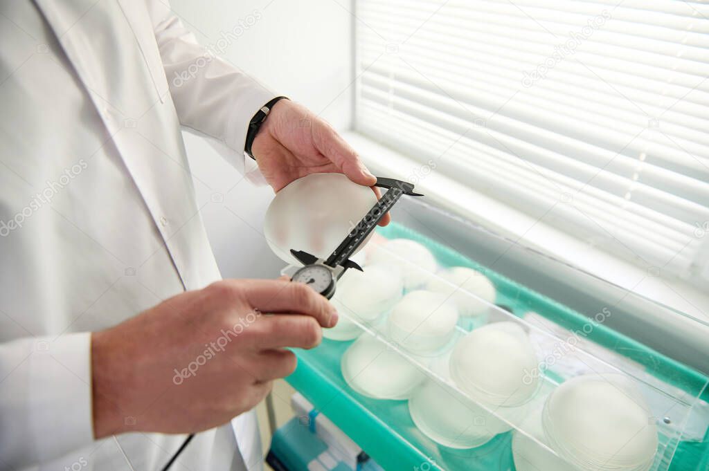 Close-up plastic surgeon hand measuring silicone breast implant size using a calliper. Mammoplasty, Breast augmentation concept. Breast prosthesis after breast removal operation due to cancer disease