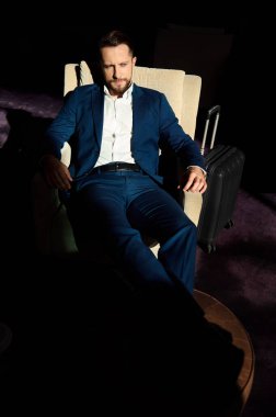 İş gezisinde başarılı genç bir iş adamının yüksek açılı görüntüsü lüks bir otelin dinlenme odasındaki bir divanda bacak bacak bacak üstüne atmış bir koltukta dinleniyor.