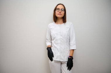Çekici güzel bir kadın, kadın doktor, sağlık çalışanı, beyaz üniformalı bir doktor fotokopi arkaplanlı beyaz duvara poz veren kameraya bakıyor.