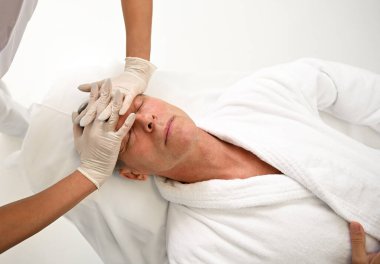 Tanımlanamayan masöz, lüks sağlık SPA merkezinde yüz masajından zevk alan yakışıklı yaşlı adamın alnına terapi amaçlı yumuşatıcı masaj yapıyor. Reklam için boşluk kopyala.