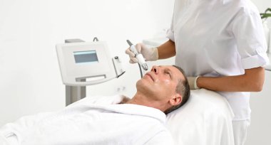 Sağlık merkezinden profesyonel cilt bakımı alan orta yaşlı bir Avrupalı adamın portresi. Yaşlanmayı önleyen, canlandıran, gençleştiren tedaviler için modern kozmetolojik tıbbi ekipmanlar