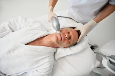 Modern sağlık merkezindeki modern tıbbi ultrasonik ekipmanlarla gençleştirici ve yaşlanmayı önleyen profesyonel tedavi gören yakışıklı ve rahat bir adamın genel bakış açısı..