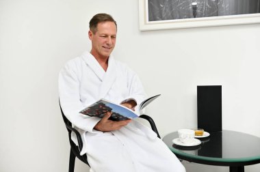 Başarılı bir orta yaşlı iş adamı, sağlık merkezinin mahremiyet odasında sıkı çalıştıktan sonra dinleniyor, erkek güzellik prosedürlerini gençleştirmek için okumadan önce dergi okurken dinleniyor.