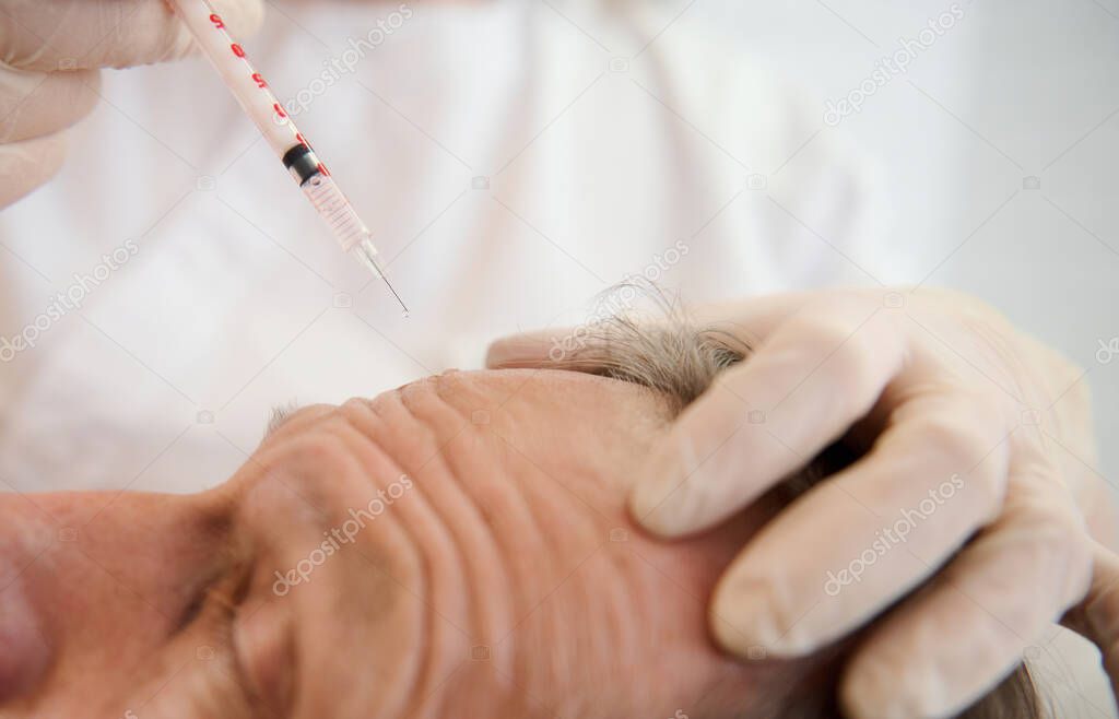 Close-up of a beautician holding a syringe and making facial injection to handsome aged man in modern spa center. Injection cosmetology, beauty rejuvenating treatment, skin and body care concept