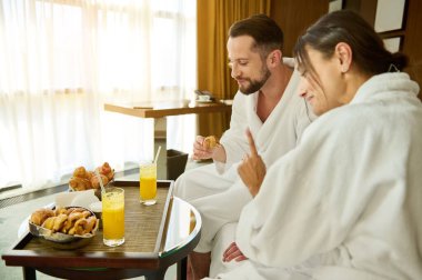 Uyandıktan sonra bornozla balayına çıkan yeni evliler kahvaltıdan sonra. Romantik bir kahvaltı. Sevecen, sevgi dolu bir çiftin otel odasında geçirdiği özel dakikaların tadını çıkarıyorlar..