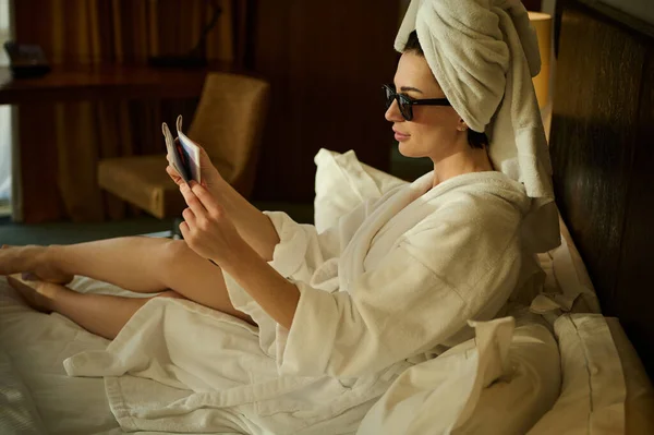 魅力的な女性 ビジネスマン リラックスした入浴後にバスタオルに包まれ 新聞を読んで 彼女の出張中にホテルの寝室のベッドに座っているのサイドポートレート — ストック写真