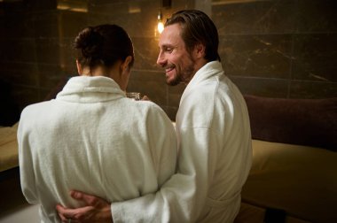 Yakışıklı, sevecen Avrupalı bir adam. Sevgili karısına sarılıyor. Güzellik merkezinde yan yana oturup dinleniyor. Mutlu yeni evliler balayında