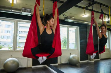 Güzel, dingin Afrikalı genç bir kadın havadan anti-yerçekimi yogası yapıyor yoga dersinde ayna yansımasına bakıyor.