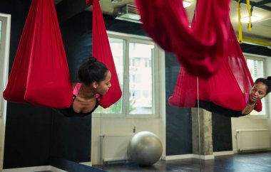 Güzel Afrikalı bir kadın jimnastik salonunda uçuş yoga esneme egzersizleri yapıyor. Spor ve sağlıklı yaşam tarzı kavramı. Yerçekimsiz havadan uçuş yoga sınıfı.