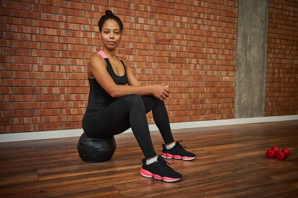 Schöne Afrikanische Athletin Stylischer Schwarzer Aktivkleidung Sitzt Auf Einem Medizinball — Stockfoto