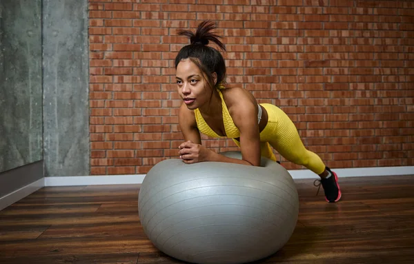 ジムスタジオでフィットネスボールで板を行う若いアフリカの女性を決定 — ストック写真