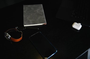 Yüksek açılı ofis aksesuarları, dizüstü bilgisayar, kutudaki kulaklıklar, saat, cep telefonu ve ahşap masadaki gri not defteri.