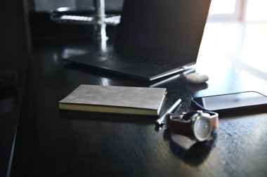Yakın plan. Ofis aksesuarları, dizüstü bilgisayarlar, kutudaki kulaklıklar, saat, cep telefonu ve ahşap masadaki gri not defteri.