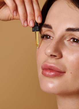 Cilt bakımı, kozmetoloji ve güzellik endüstrisinde bitki bazlı güzellik ürünleri kullanılıyor. Kafkasyalı genç bir kadının taze cilt için yüzüne damlatan bir damlacıkla gerekli yağı damlattığı yakın plan.