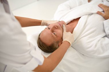 Tanımlanamayan bir estetisyen, olgun bir adamın yüzüne yaşlanma karşıtı masaj yapıyor. Sağlık kaplıcalarında cilt bakımı ve erkek güzellik prosedürleri kavramı