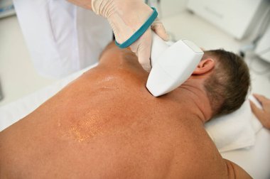 Spa kliniğinde radyo dalgası kaldırma. Sağlık kaplıcasının arkası yakın plan erkek müşterisi modern tıbbi ekipmanlarla profesyonel vücut tedavisi görüyor. Vücudun ultrasonik boşaltımı için aparat.