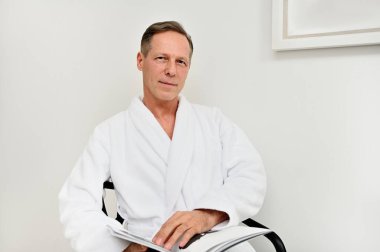 Yakışıklı, çekici, beyaz atlı beyaz bornozlu beyaz bir adam elinde bir dergi ile koltukta oturuyor, kameraya bakıyor, lüks sağlık merkezinin mahremiyet odasında dinleniyor.