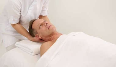 Yakışıklı, olgun, beyaz bir adamın masaj masasında dinlenirken profesyonel yüz kaldırma masajı yaptırdığı yakın plan. Yaşlanma önleyici, gençleştirme, yüz gerdirme ve cilt bakımı konsepti