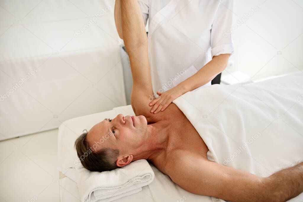 Mature Caucasian man receiving professional therapeutic rehabilitative massage at wellness clinic. Body care, physiotherapy, sport injury rehabilitation concept, holistic care concept