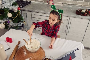 Avrupalı güzel bir çocuğun en güzel görüntüsü, kafasında elf halkası olan sevimli bir kız, cam bir kâse ile unu karıştıran küçük bir blog yazarı, noel kurabiyeleri ve ekmek için hamur hazırlıyor.