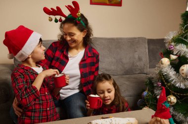 Güzel, sevecen anne ve onun sevimli oğlu ve kızı masada oturup evde lokumlarla sıcak çikolata içiyorlar. Mutlu Noeller.
