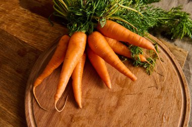Büyük bir demet taze havuç, yeşil tepeler ve tahta kesme tahtasının üzerinde yapraklar. Mevsimlik çiğ sebzelerin besin kaynağı. Uzayı kopyala
