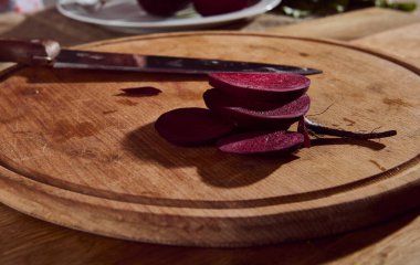 Yemek arkaplanı. Tahta kesme tahtası ve mutfak bıçağı üzerinde kırmızı pancar dilimleri yakın plan..