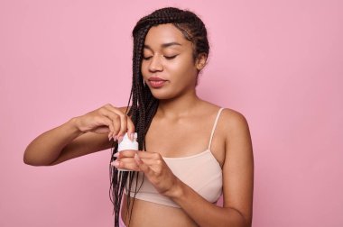 Afrikalı güzel bir kadın beyaz bir konteynırı ilaç ya da vitaminle açıyor. Sağlık ve tıbbi içerik, pembe arka planda fotokopi alanı ile güzellik tedavisi kavramı