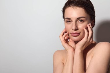 Yakın plan. Sağlıklı, taze tenli, çekici, çıplak, doğal, güzel bir kadın ellerini yüzüne koyar, izole, beyaz bir arka plan. Uzayı kopyala Kozmetik, güzellik, cilt bakımı, cilt bakımı