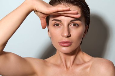 Yakın plan. Kafkasyalı zarif bir kadının elleriyle yüzüne dokunup kameraya baktığı yüz gerdirme ve kaplıca tedavisi için düzgün masaj hareketleri yaptığı güzel bir yüz resmi. Kozmetoloji