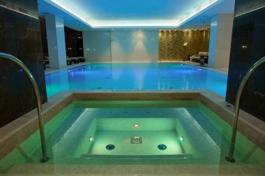 Sualtı ışıkları ve şelaleli termal yüzme havuzu lüks otel spa merkezinde.