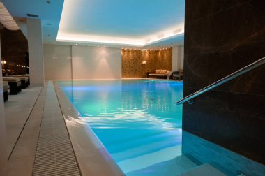 Su altı ışıkları ve şelaleli termal yüzme havuzlu sağlıklı bir spa merkezinin lüks modern iç tasarımı.