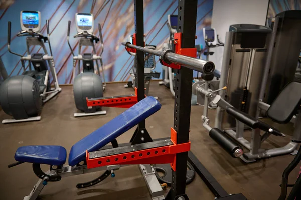 Photos of the interior of the gym with a bench press, an iron barbell, dumbbells, weights and exercise machines.