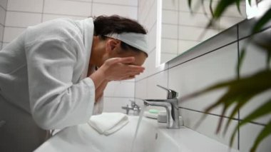 Güzel bir kadın yüzünü yıkıyor, makyaj malzemelerini ev banyosunda nemlendirici kozmetik malzemelerle temizliyor. Cilt bakımı, ev güzellik prosedürleri, saflık temizliği ve hijyen konsepti..