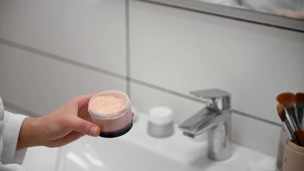 Close-up. Womans hands holding a makeup brush and applying a mattifying facial powder to it in the bathroom