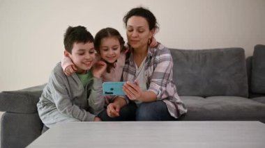 Sevgi dolu anne, oturma odasında tatlı çocuklarının yanında oturmuş elinde akıllı bir telefonla bir video görüşmesinde konuşuyor..