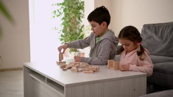 Imádnivaló Koncentrált Kaukázusi Gyerekek Ülnek Asztalnál Társasjátékoznak Tornyot Építenek Fatömbökkel — Stock videók