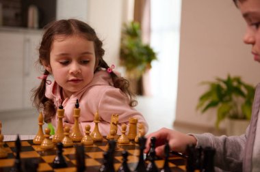 Satranç taşını eline alıp hamlesini yapan ağabeyi ile satranç oynayan güzel bir Avrupalı kızın yakın plan portresi. Çocuklar için entellektüel akıllı geliştirme masa oyunları